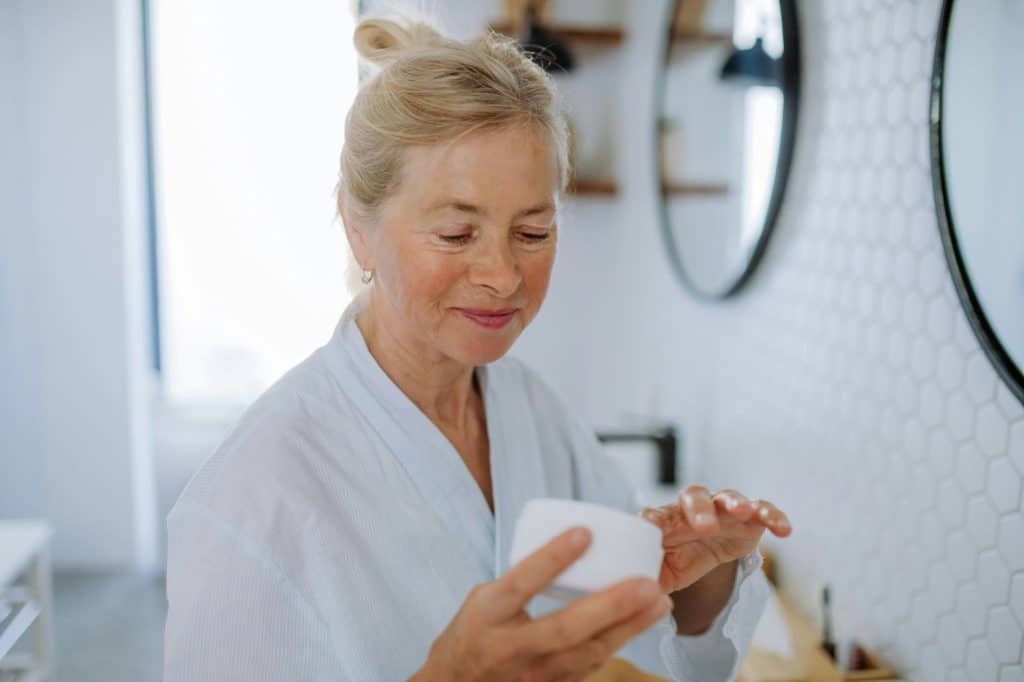Personne dans sa salle de bain applicant un produit beauté