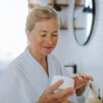 Personne dans sa salle de bain applicant un produit beauté