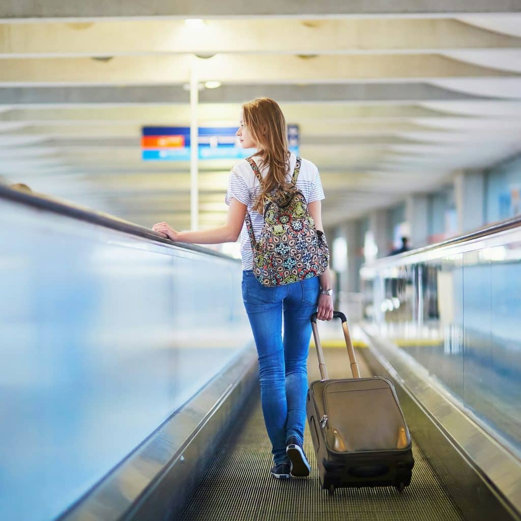 Femme avec valise qui emprunte un tapis roulant